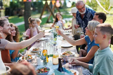 multi generational family enjoying a meal at a table outside and raising glasses to celebrate