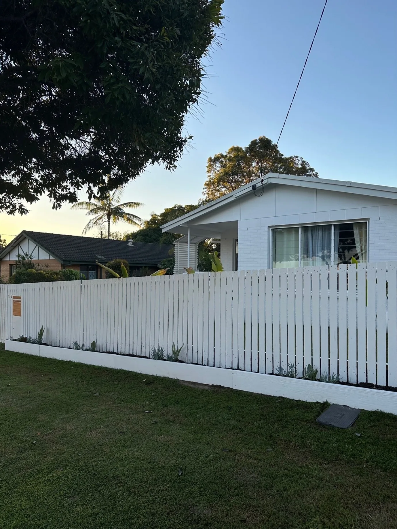 side view of newly installed and painted front fence, with white painted house behind it this end result is the perfect cheap fence idea for front yard