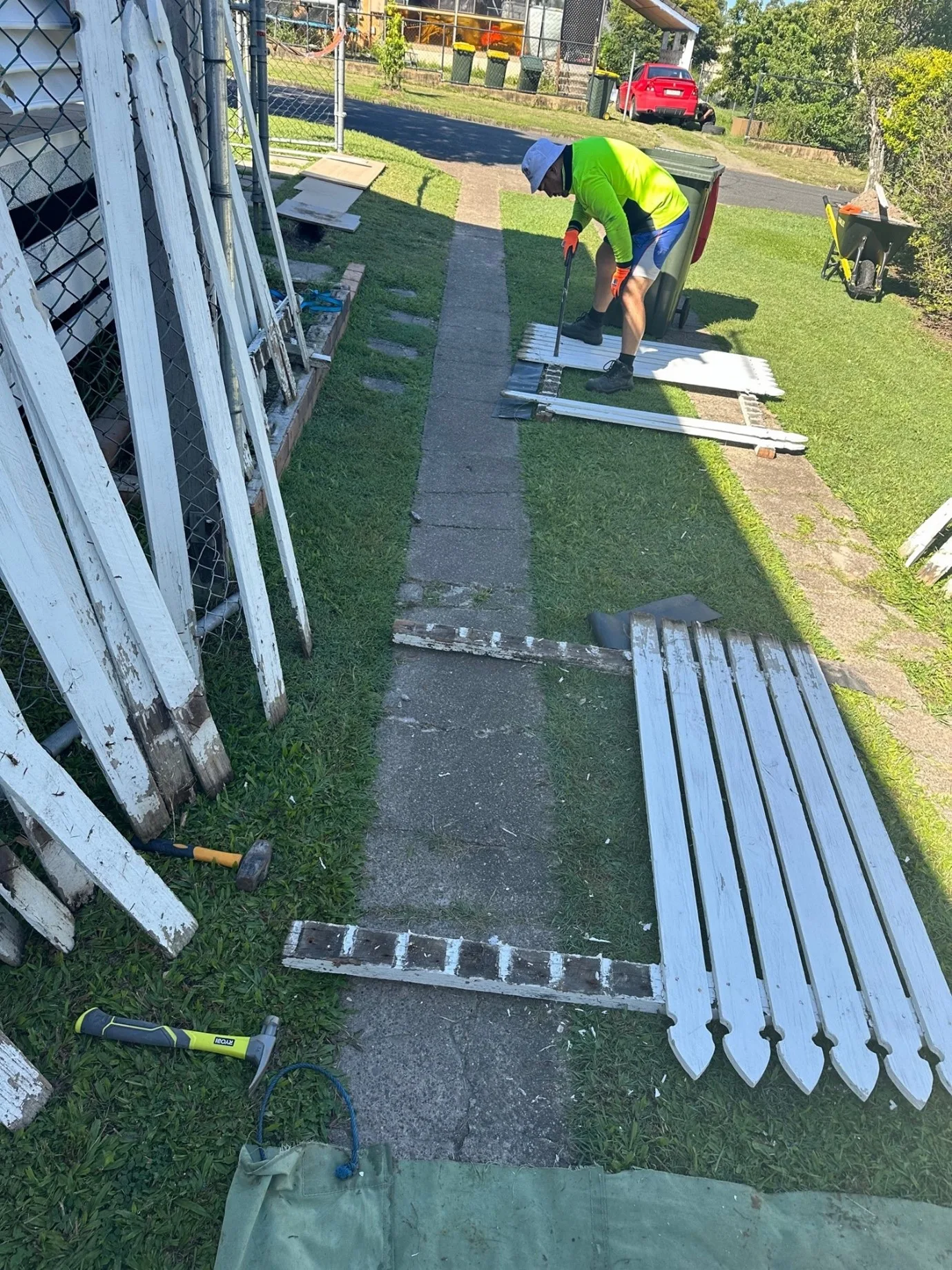 man fixing a second-hand fence with palings on the ground and stacked up no side wall is the perfect cheap fence idea for front yard