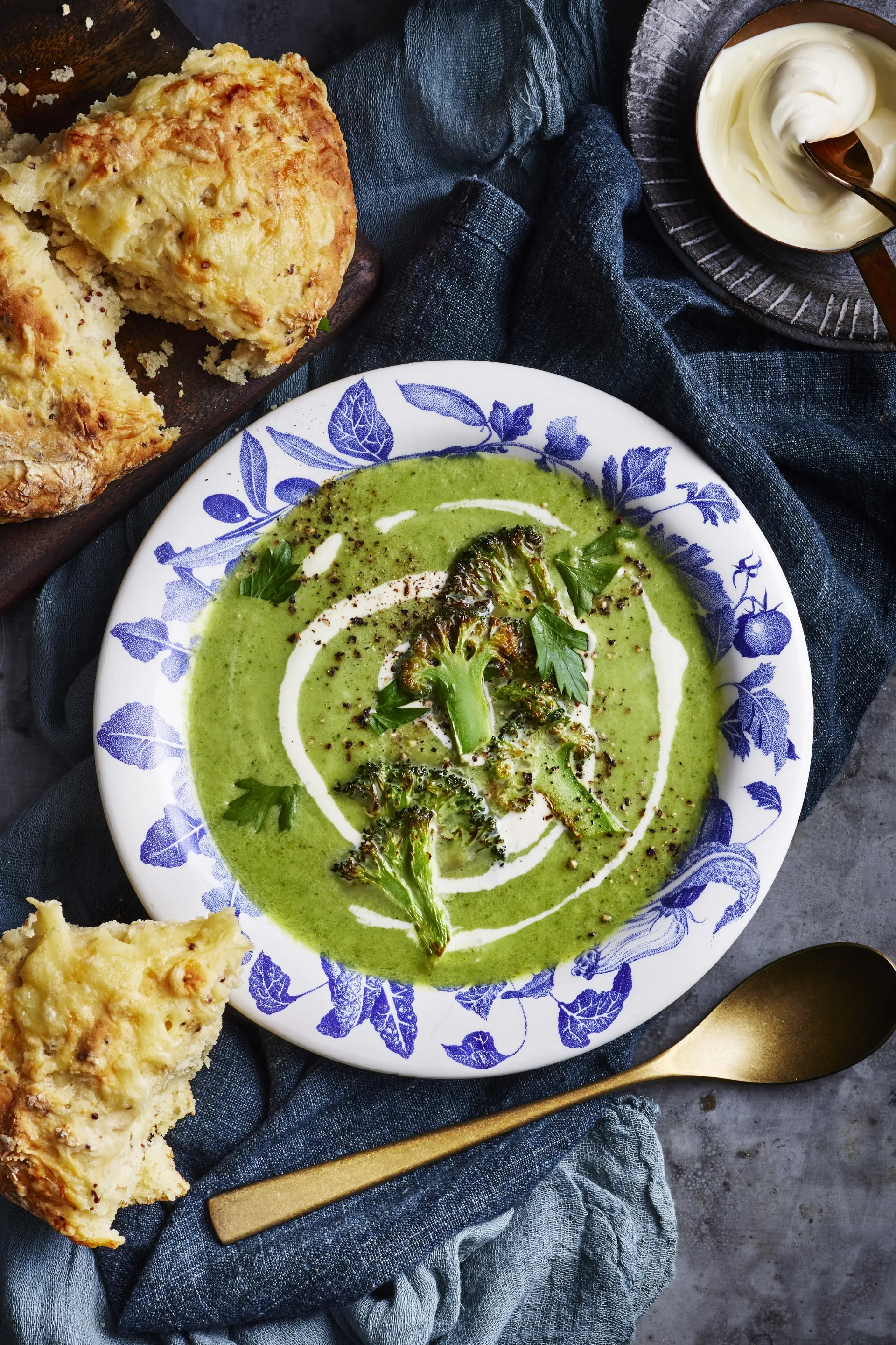 broccoli soup in blue bowl with scones surrounding it