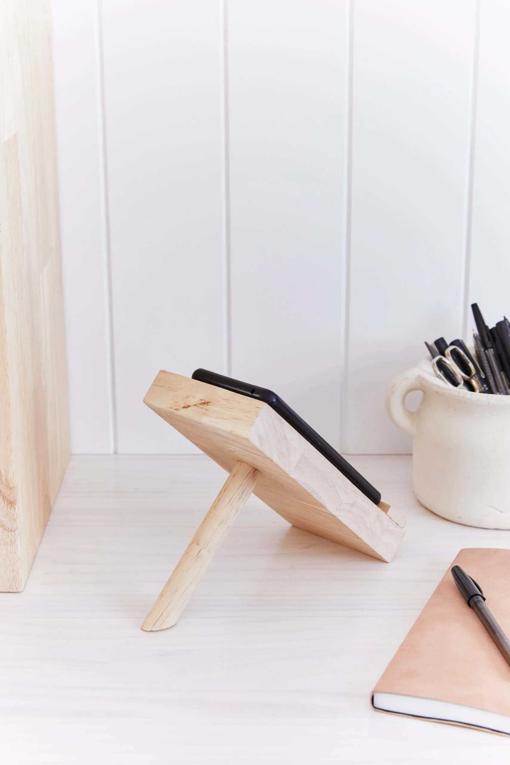 Escritório em casa montado com suporte de telefone de madeira virado para o lado e pote de lápis