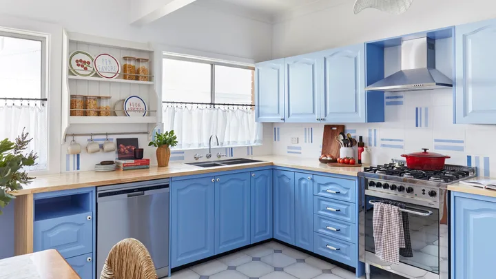 A bright kitchen with blue cabinets, stainless steel appliances, a wooden countertop, and decorative plates on shelves.
