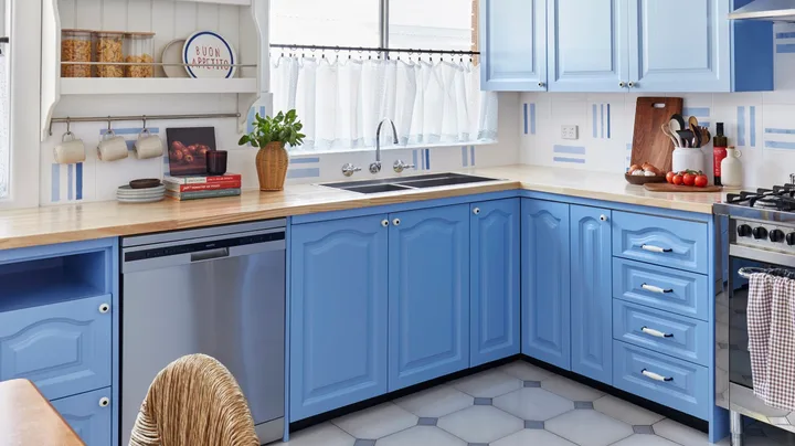 A bright kitchen with blue cabinets, stainless steel appliances, a wooden countertop, and decorative plates on shelves.