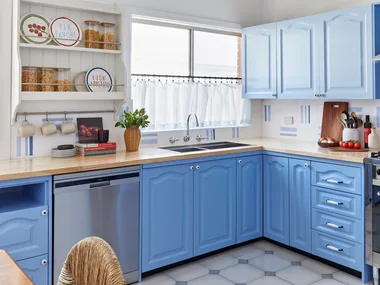 A bright kitchen with blue cabinets, stainless steel appliances, a wooden countertop, and decorative plates on shelves.