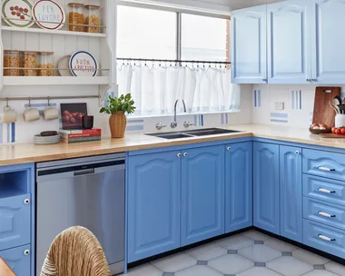 A bright kitchen with blue cabinets, stainless steel appliances, a wooden countertop, and decorative plates on shelves.