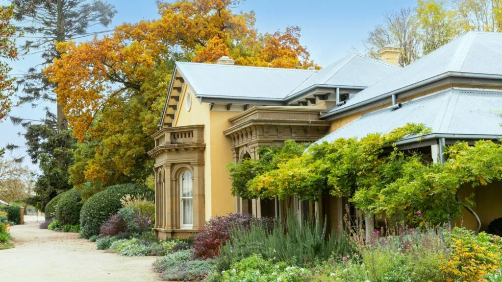 homestead facade made of yellow stone with hedging and plants around it