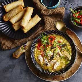 bowl of chicken and corn soup with spring rolls on the side