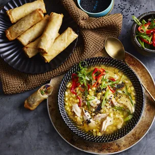 bowl of chicken and corn soup with spring rolls on the side