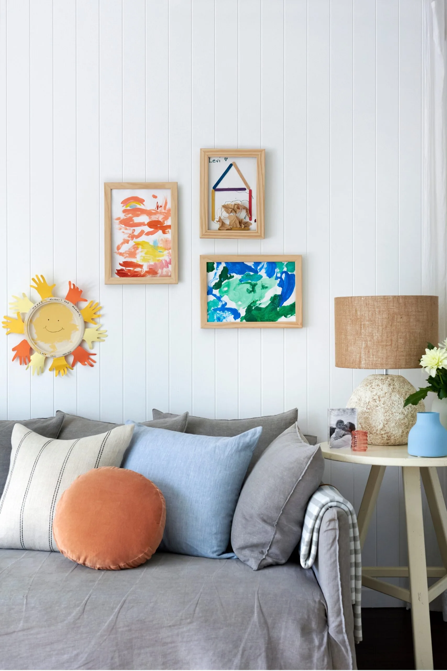 couch with several cushions and art frames above that showcase kids fingerpaintings