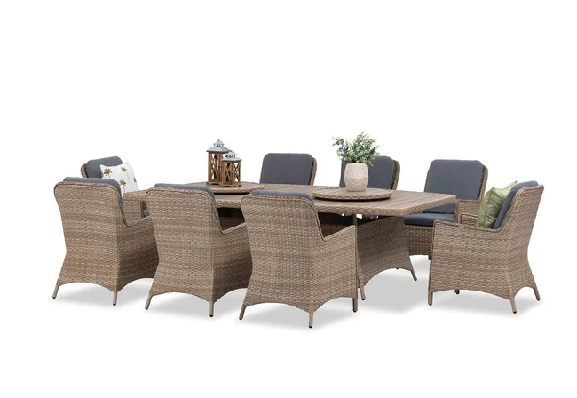 Outdoor wicker dining set with eight chairs, cushions, rectangular table, lanterns, and a potted plant centerpiece.
