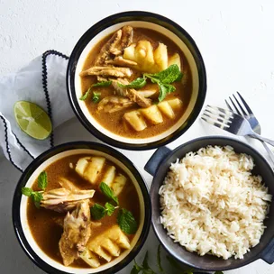 Two bowls of fish curry with pineapple and mint, served with a side of white rice and a lime wedge.