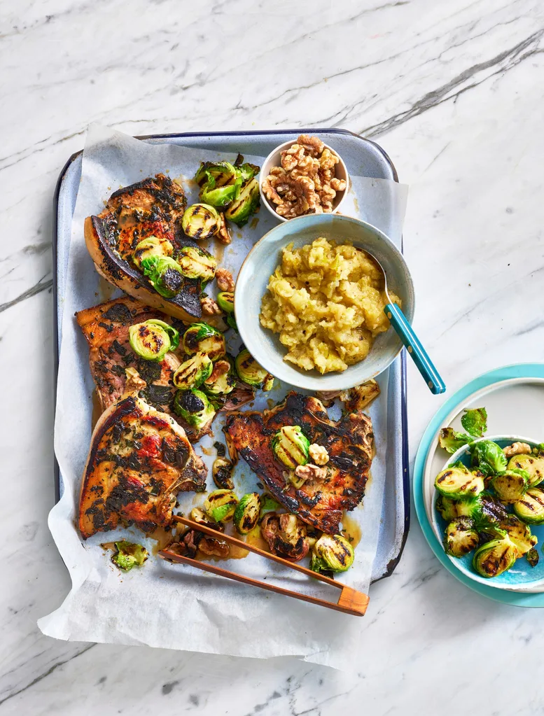 tray bake with pork chops, bruseel sprouts and apple sauce in a bowl on it