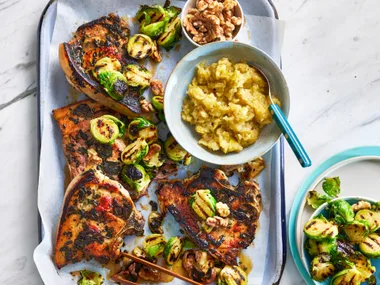 tray bake with pork chops, bruseel sprouts and apple sauce in a bowl on it