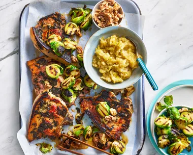 tray bake with pork chops, bruseel sprouts and apple sauce in a bowl on it