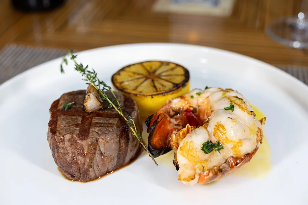 fine dining surf and turf with balmain bug curled on one side and piece of filet mignon with burnt lemon half in background