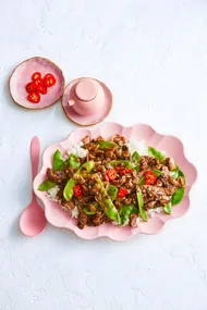 beef and black bean stir fry with snap peas and chili on top in scalloped pink bowl