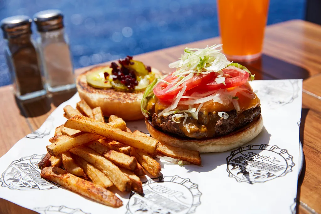 picture of open faced burger with tomato and lettuce on top. stack of handcut chips on the side with salt and pepper shakers blurred into background