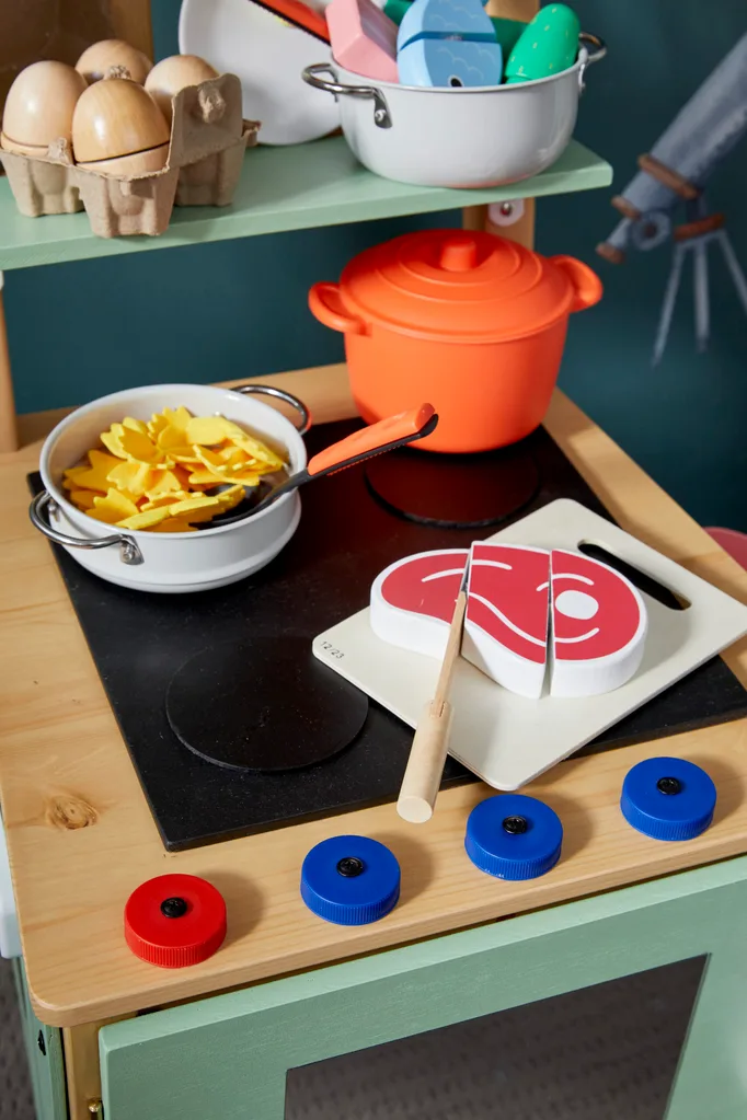 close up of fake stovetop with plastic pasta in a pot and a wooden steak precut into three pieces