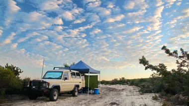 car with gazebo behind it and camping set-up with blue sky and lots of clouds in the background