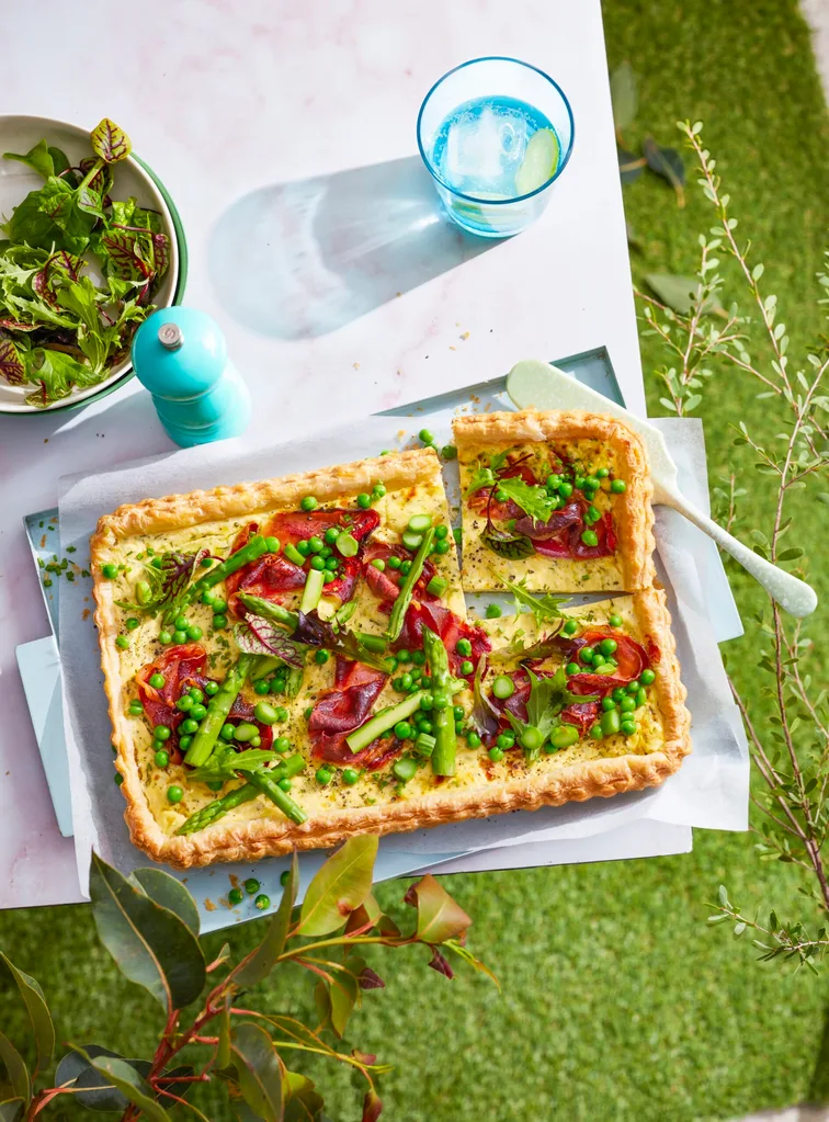 birds eye view of asparagus quiche with blue glass behind and herbs on top