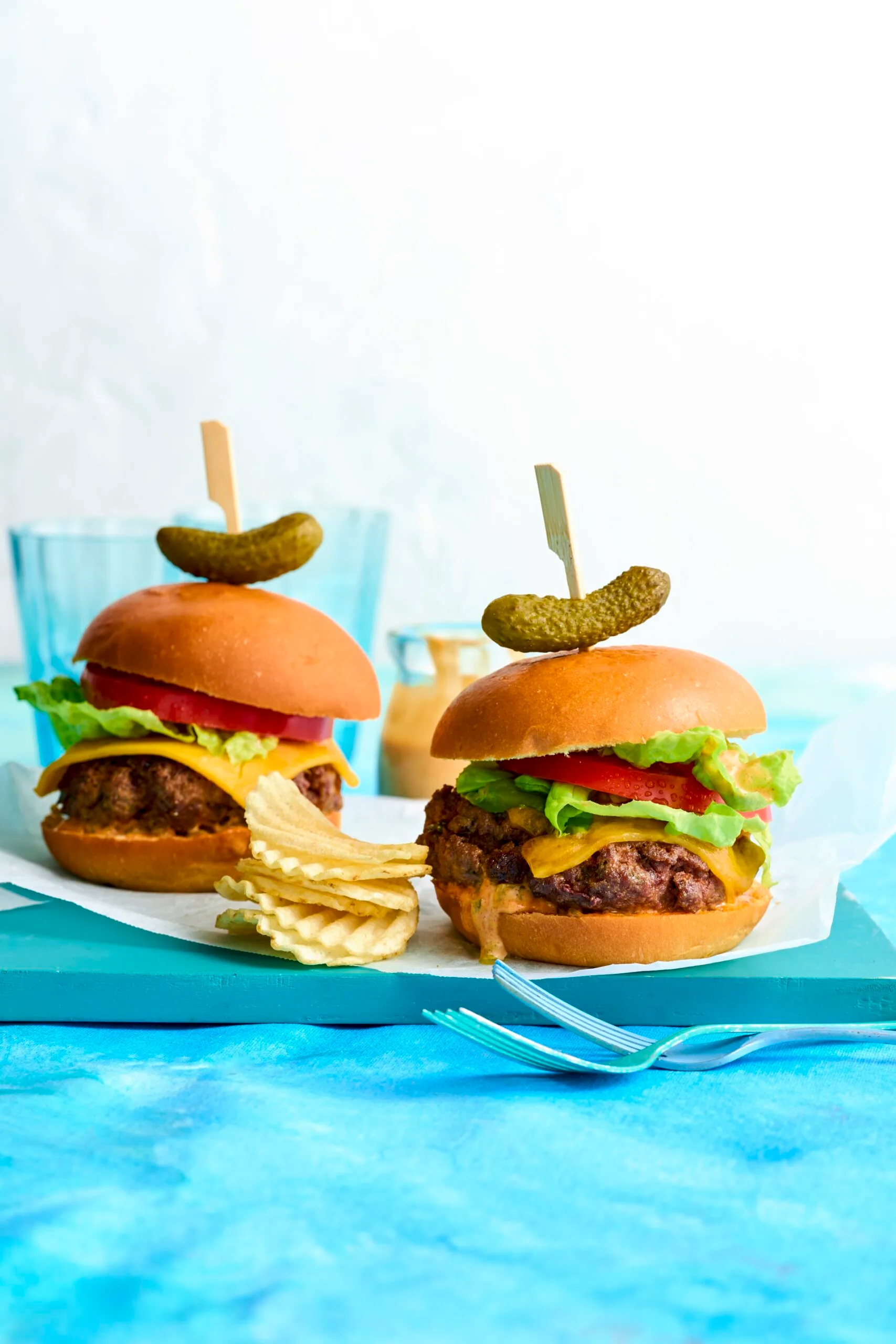 beef burger with pickle on top on blue tabletop