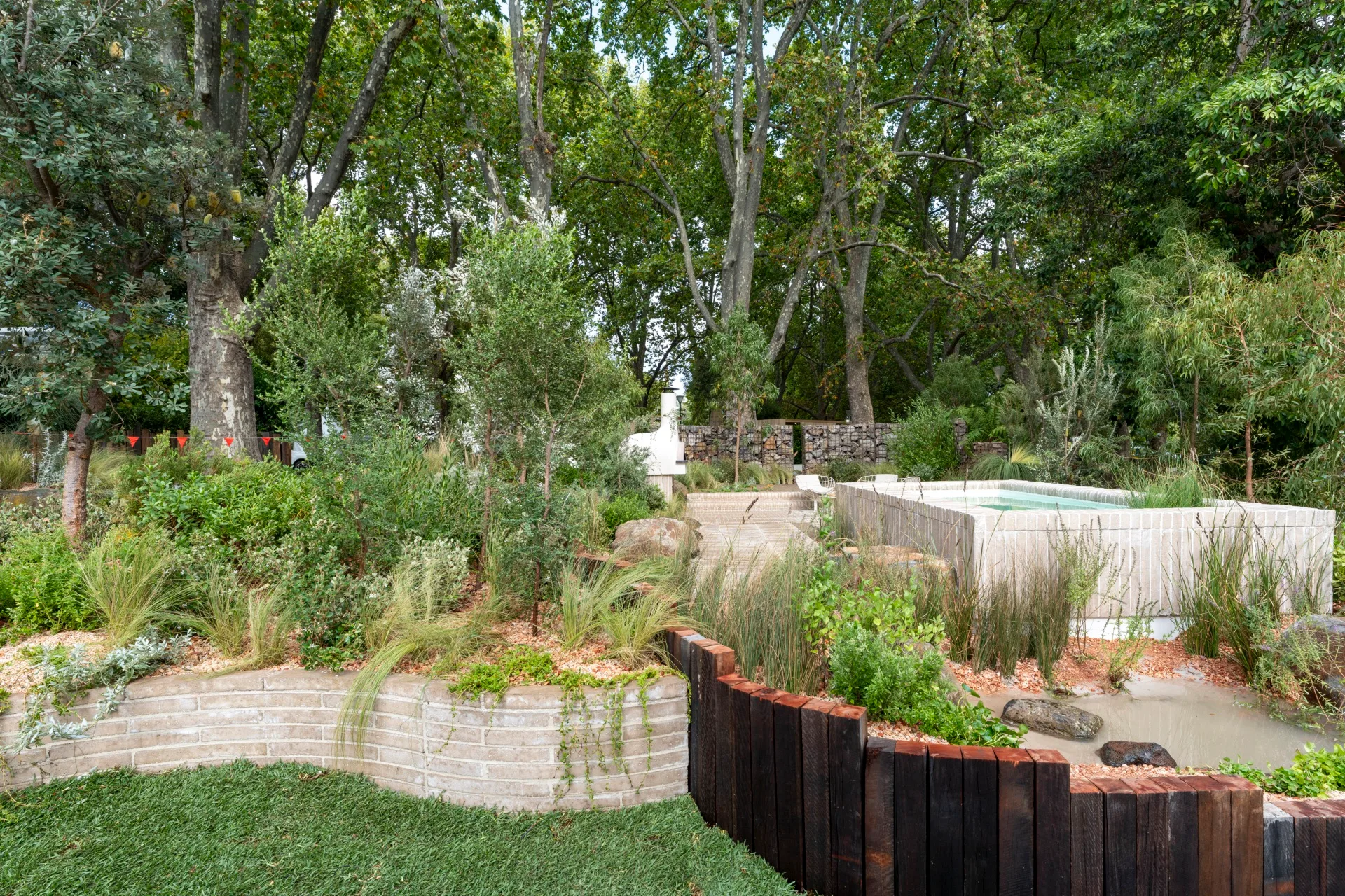garden made up of recycled material with flowing plants over garden beds and a small pool on the left hand side