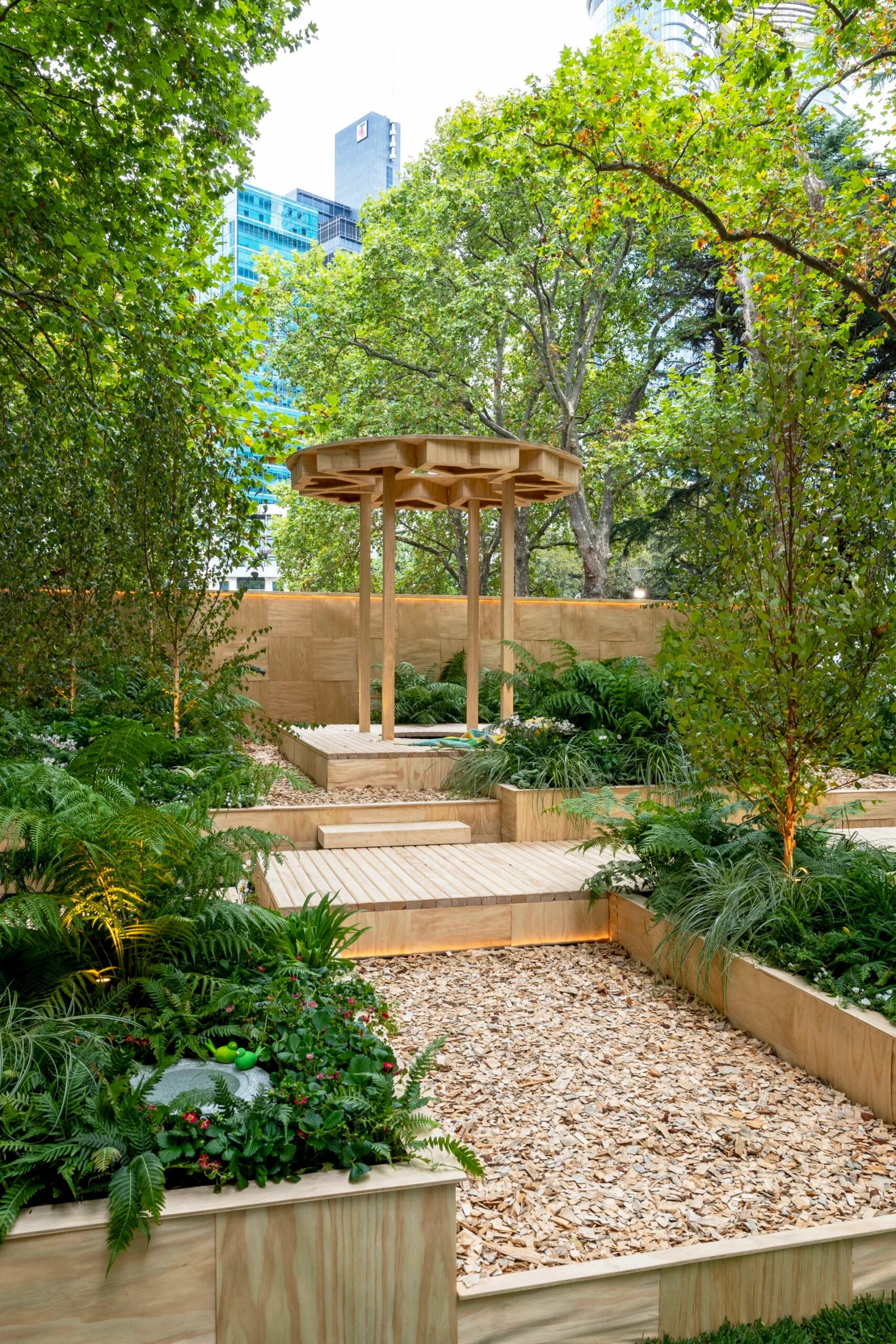 pavilion on terraced garden with bark chip pathway and shade loving ferns in garden beds on either side
