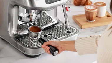 Person using Breville espresso coffee machine with latte next to the machine on the bench.