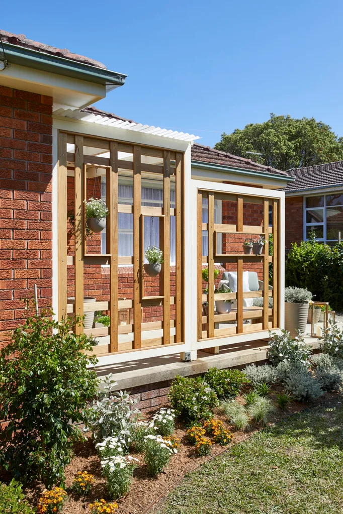 front garden with daisies in front of porch and vertical wooden screening with a couple of hanging plants