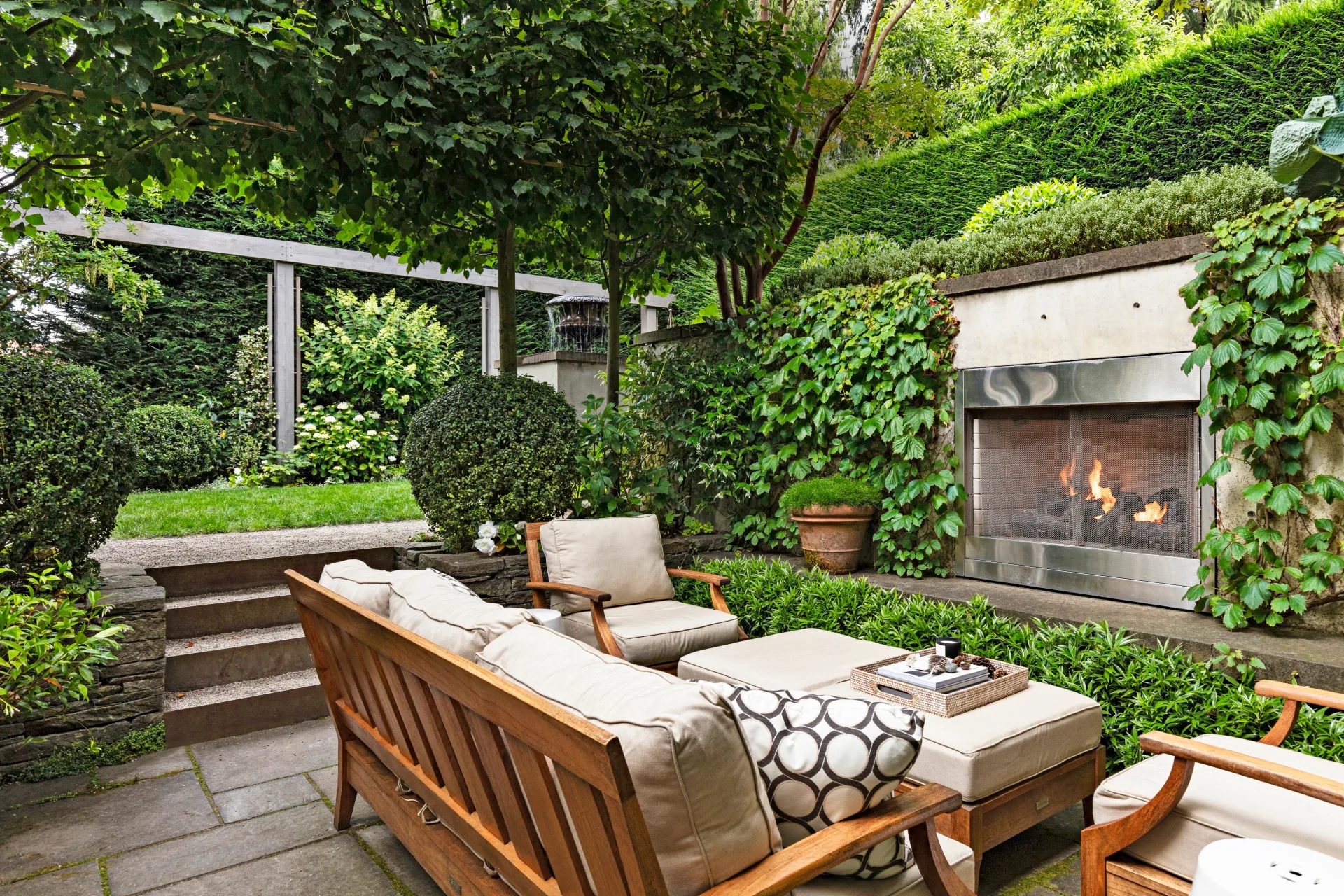 outdoor fire built into wall in sunken outdoor seating area with surrounding hedge and small set of steps going up to lawn