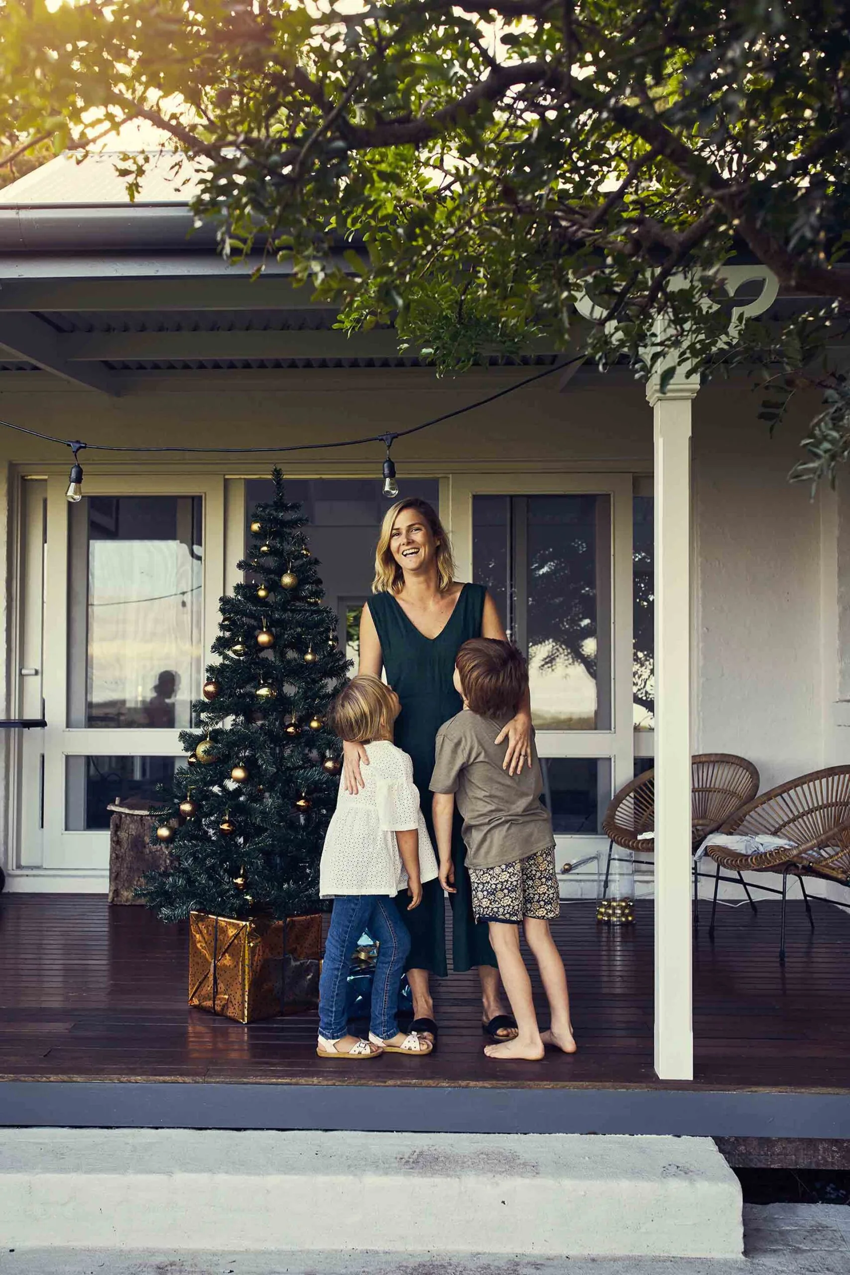 Woman hugging two kids on a verandah with Christmas decorations on it