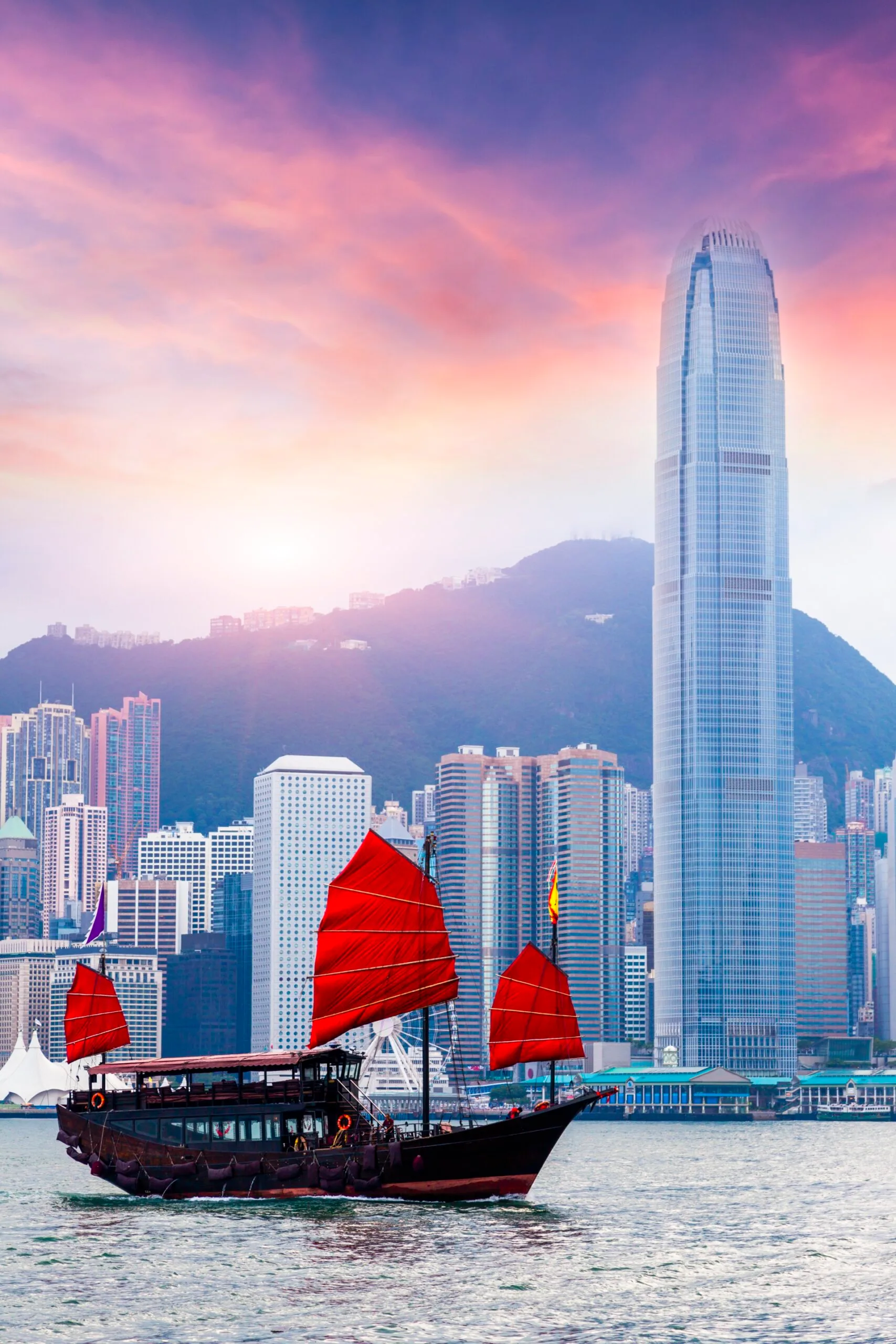 red traditional hong kong boat with red sails sailing in front of hong kong skyline