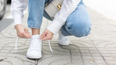 Person kneeling down and tying the shoelaces on their crisp white shoes