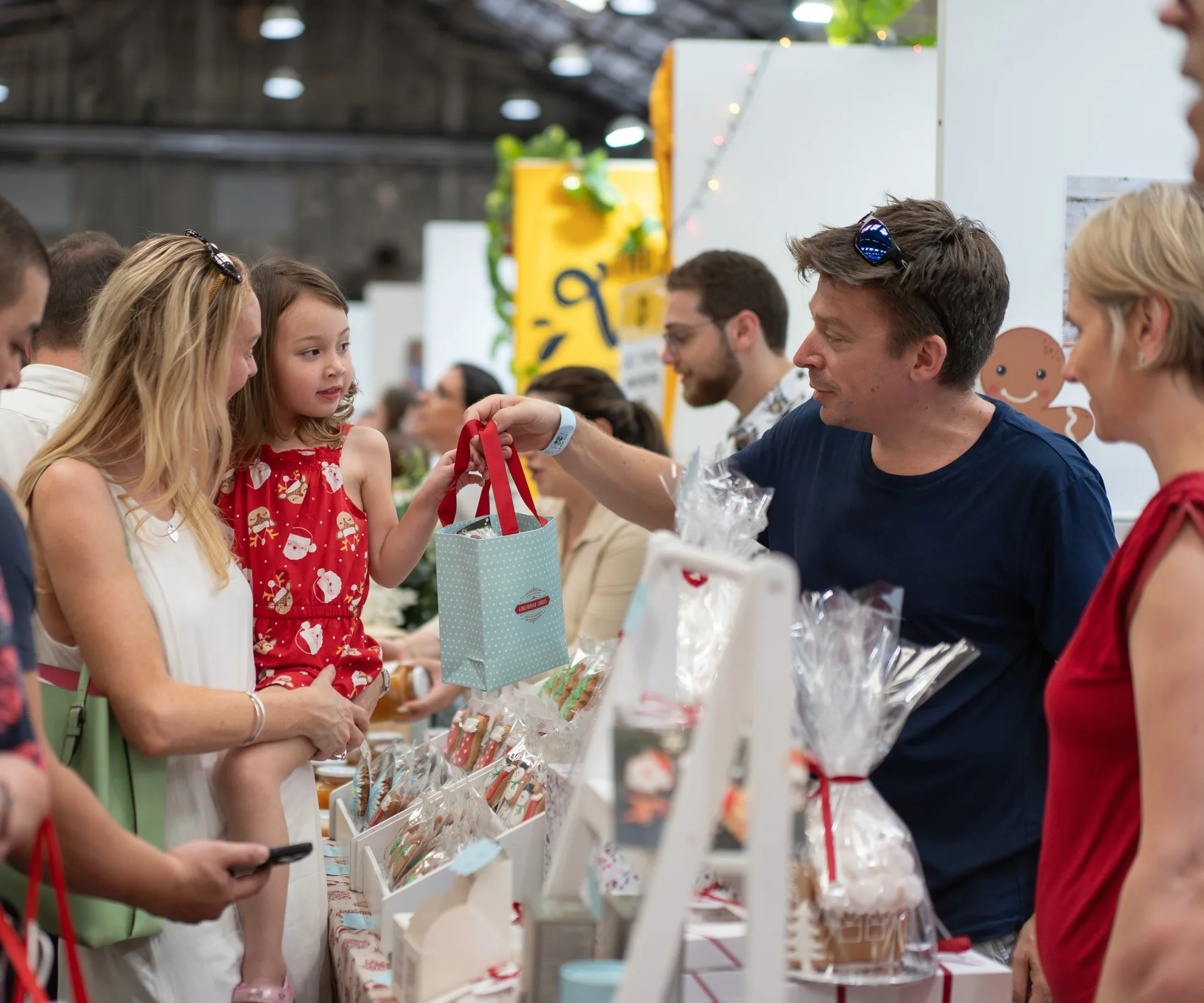 child being carried and handed christmas bag present from stallholder at christmas market in melbourne