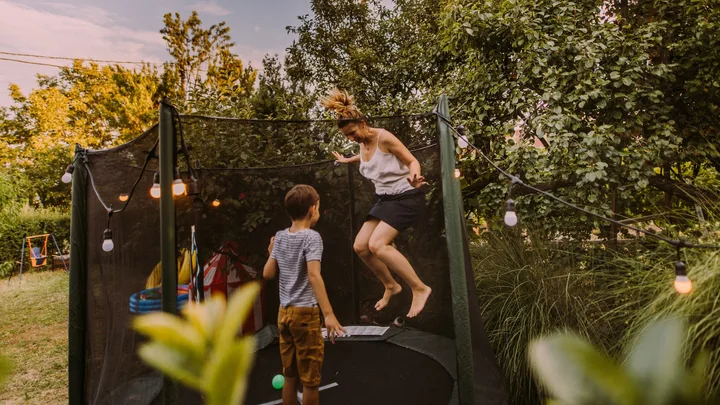 A mother and child bouncing on a trampoline in the backyard.