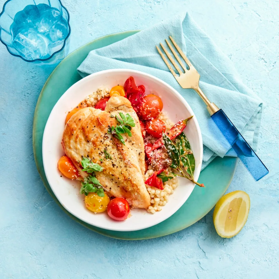 pan fried chicken in bowl with couscous vegetables against a blue background