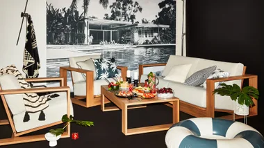 Modern living area with wooden furniture, a pool mural, and a coffee table with assorted snacks and drinks.
