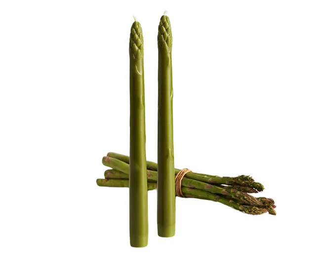 Two candles shaped like asparagus standing beside a bundle of real asparagus spears.