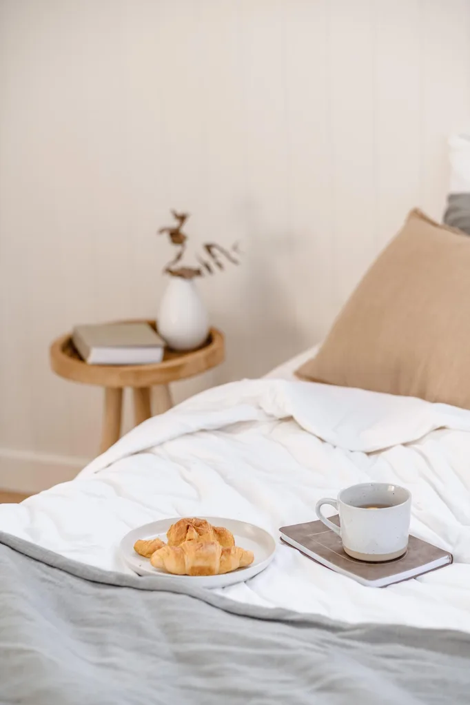 A calming coastal style bedroom with a plate or croissants and a cup of coffee