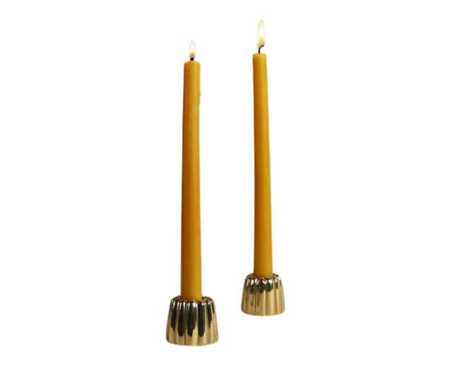 Two lit yellow candles with metal holders on a white background.