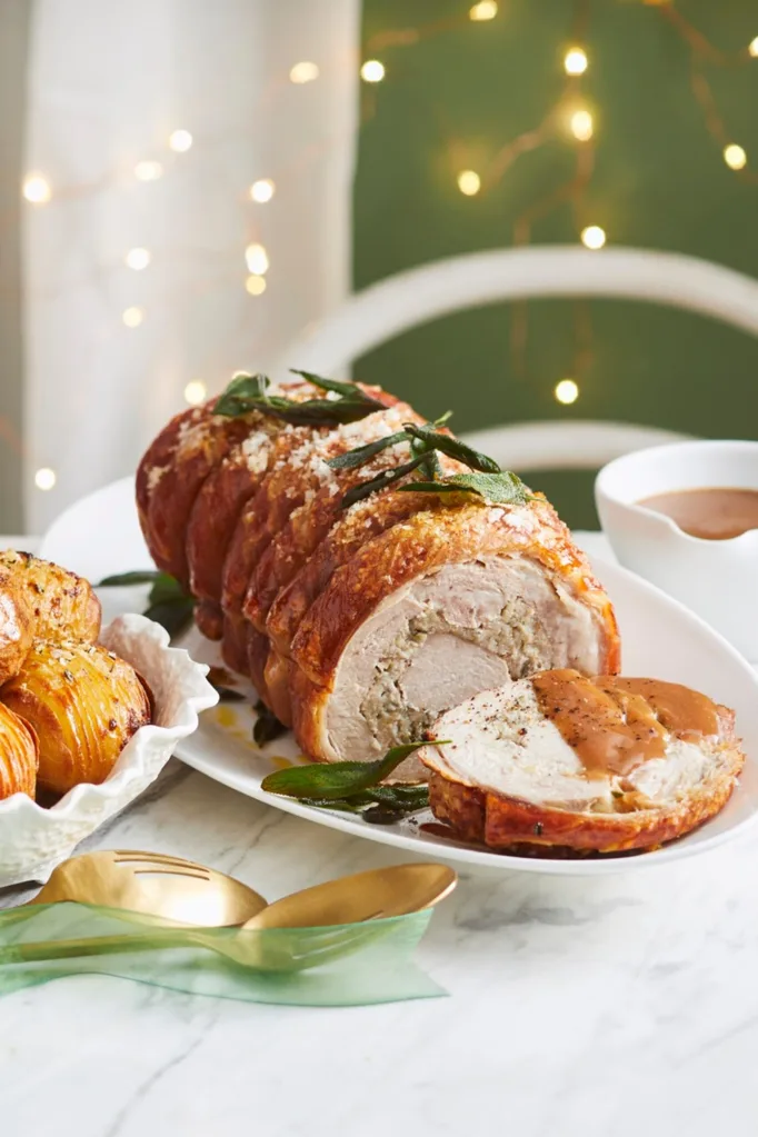 roast crackling pork with sage leaves on top and Hasselback potatoes in bowl on the side