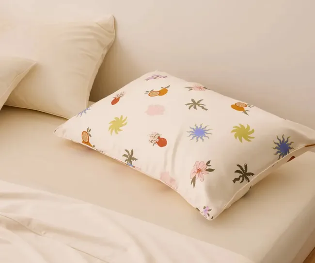 Decorative pillow with colorful floral and fruit patterns on a beige bed.