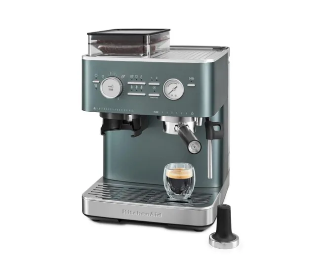 Silver KitchenAid espresso machine with a small cup of espresso on the drip tray and a tamper beside it.