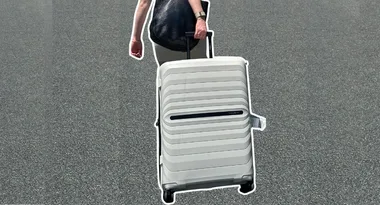 Person pulling a white suitcase on wheels along a paved surface.