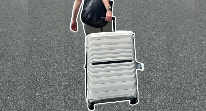 Person pulling a white suitcase on wheels along a paved surface.