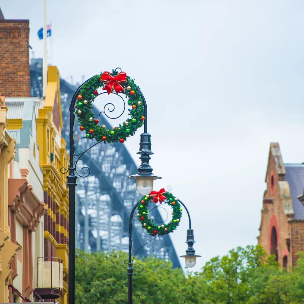 image of light poles with wreaths hanging off them at the rocks christmas market sydney with harbour bridge in the background