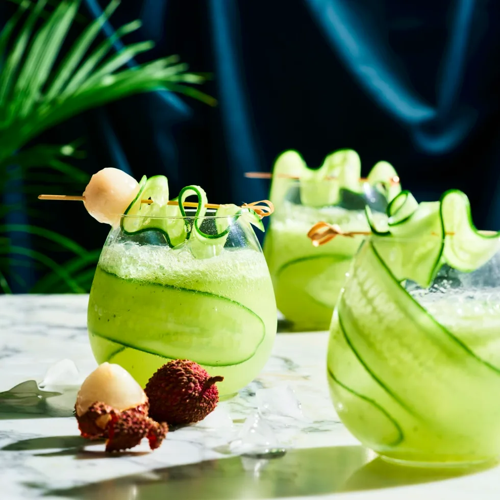 cucumber spritz with cucumber sliver wrapped around stemless wine glass with lychee on skewer over the top