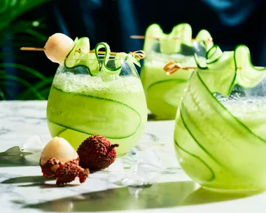 cucumber spritz with cucumber sliver wrapped around stemless wine glass with lychee on skewer over the top