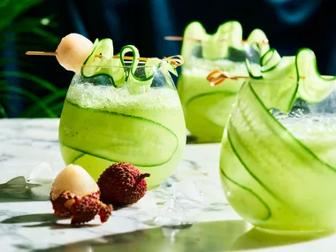 cucumber spritz with cucumber sliver wrapped around stemless wine glass with lychee on skewer over the top