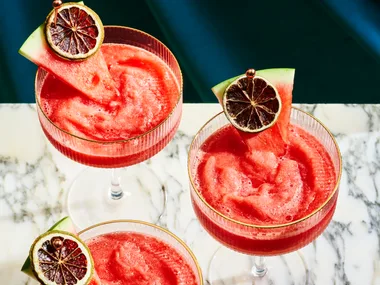 3 watermelon daiquiri's on a marble board, with a wedge of watermelon and a dried lime ontop of the cocktail as a garnish